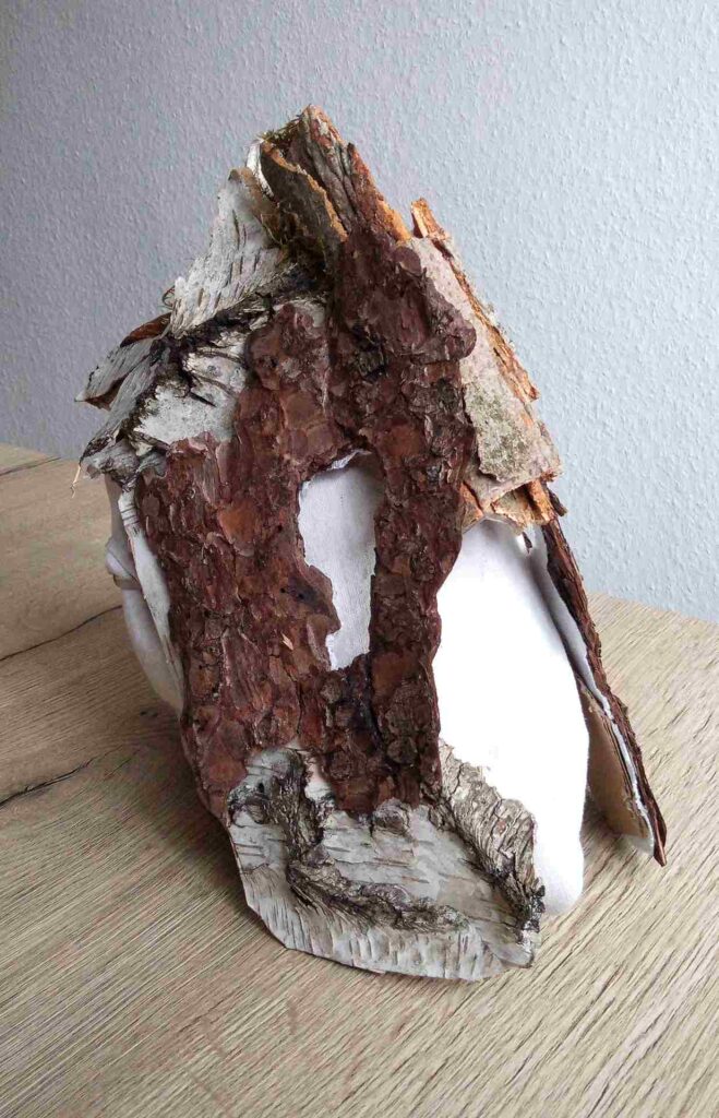 Tobias Funk. 2022. Der Geist der wachsenden Erkenntnis (Ansicht 7). Skulptur, alte Rinde von Birke, Buche, Fichte (Fundort: Marburg), Moos, auf alten Leinenstoff, Restpappe. Verklebung mit Holzleim. Halterung aus verknoteten Bändern alter FFP2 Masken. Innen mit Monogramm gestempelt und Entstehungsjahr versehen. 19,4 x 34,2 x 17,6 cm